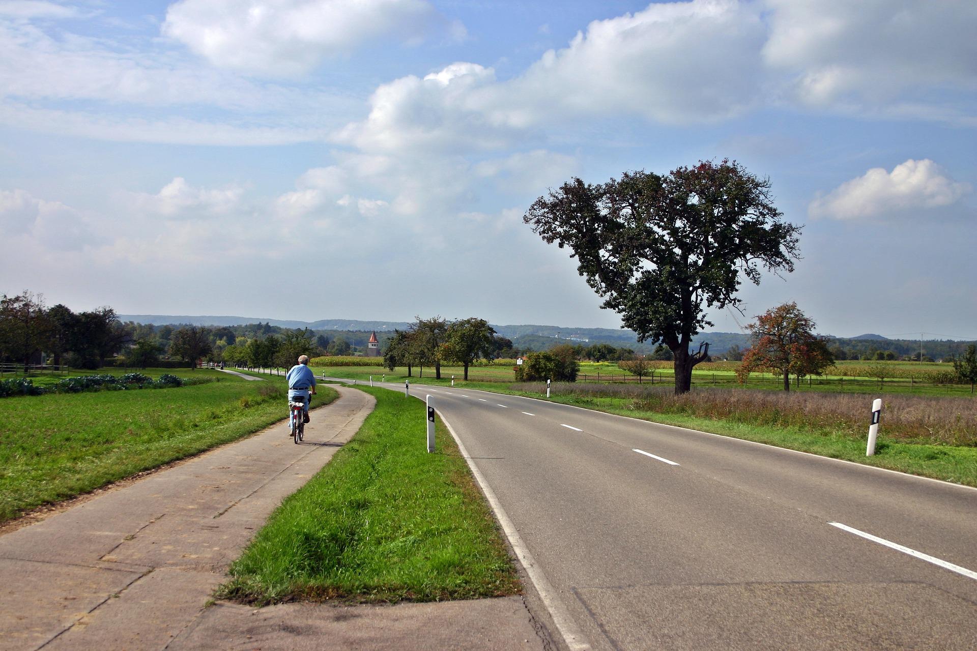 Eine Landstraße mit separatem Radweg auf dem ein Radfahrer fährt.