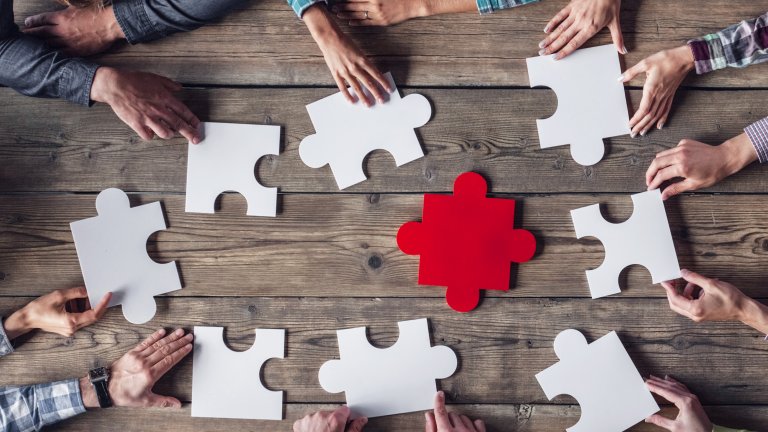 Partner werden Tisch von oben mit übergroßen Puzzleteilen und Händen die danach greifen